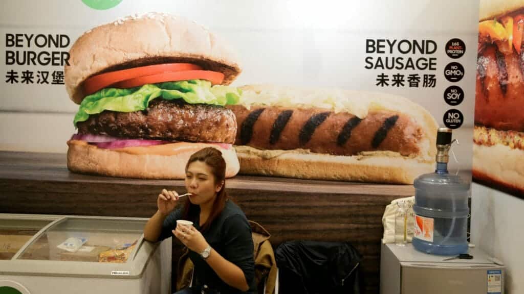 FILE PHOTO: A woman sits next to a poster at the booth of plant-based food company Beyond Meat at VeggieWorld fair in Beijing, China November 8, 2019. Picture taken November 8, 2019. REUTERS/Jason Lee/File Photo