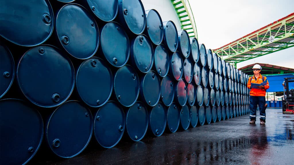 Нефтяник идет вдоль бочек с нефтью