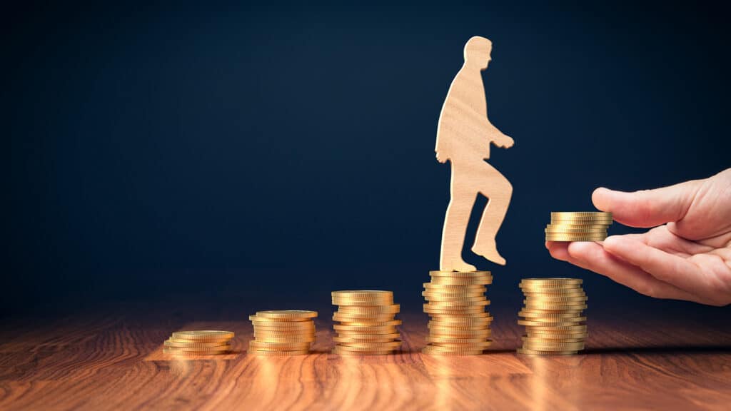 Return on investment, growing savings or wage income concept. Coins and wooden person going on increasing columns of coins. Helping hand adds more money. Successful investment concept.