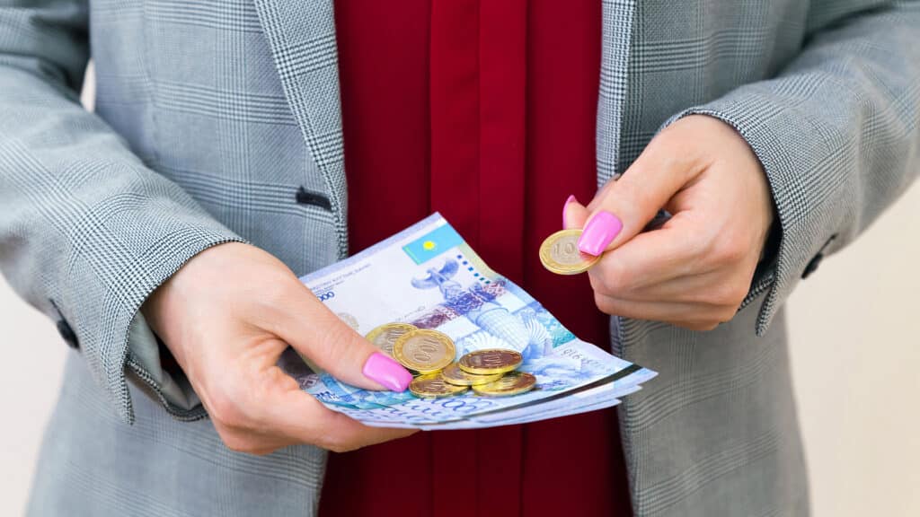 Closeup of woman's hands holding kazakhstani tenge banknotes and coins. Spending and saving concept