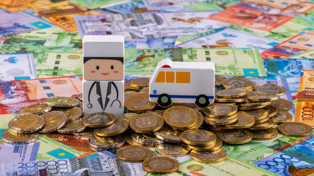 Symbolic figurine of a doctor and an ambulance against the background of Kazakhstani money (tenge)