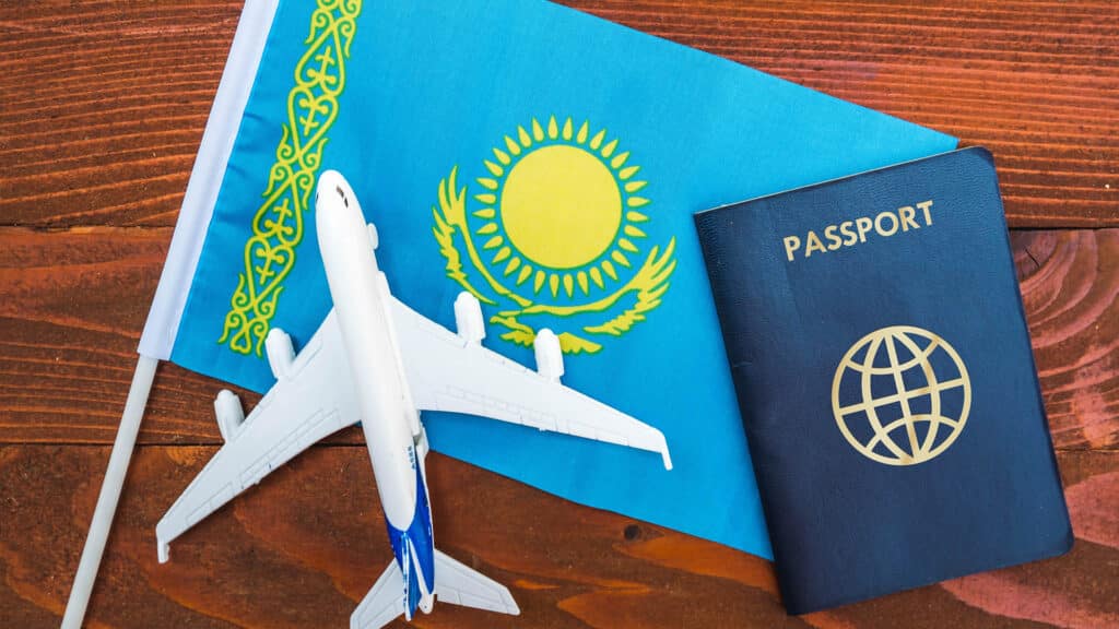 Flag of Kazakhstan with passport and toy airplane on wooden background. Flight travel concept