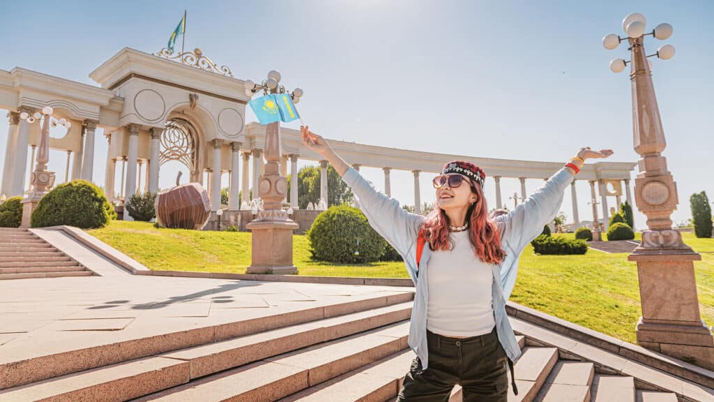 Young woman tourist holding a small Kazakhstan flag in First President's Park in Almaty